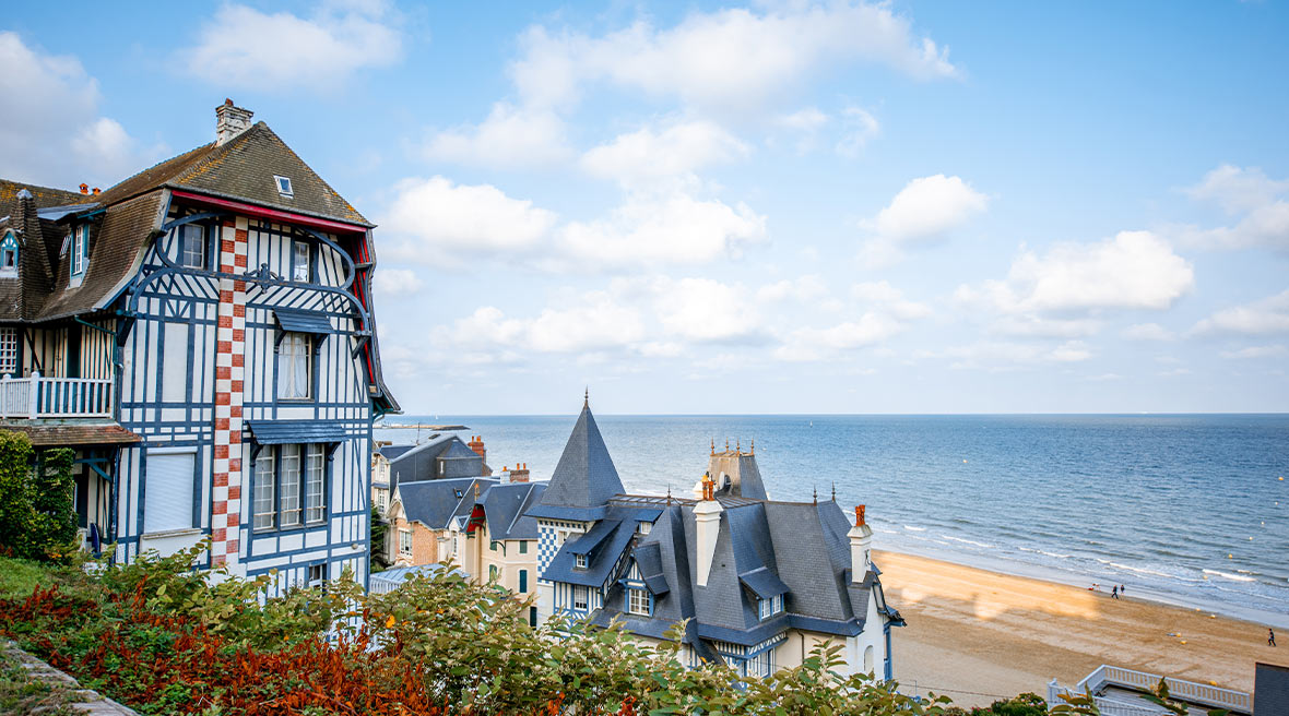 Pretty French houses with a path leading down to a sandy stretch of beach under blue skies